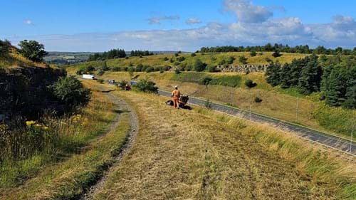 An engineer in PPE accompanies the robot cutter on a sweep of grass by the A56