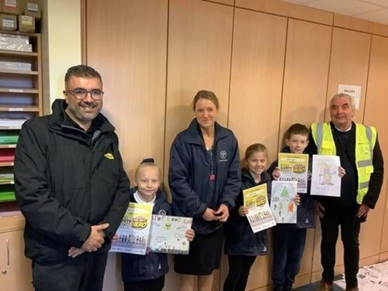 Three adults standing with the three winning children holding the posters they created.